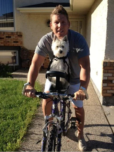 Person riding a bike with their small dog safely secured in the Buddyrider bicycle pet carrier attached to the bike's seat post.
